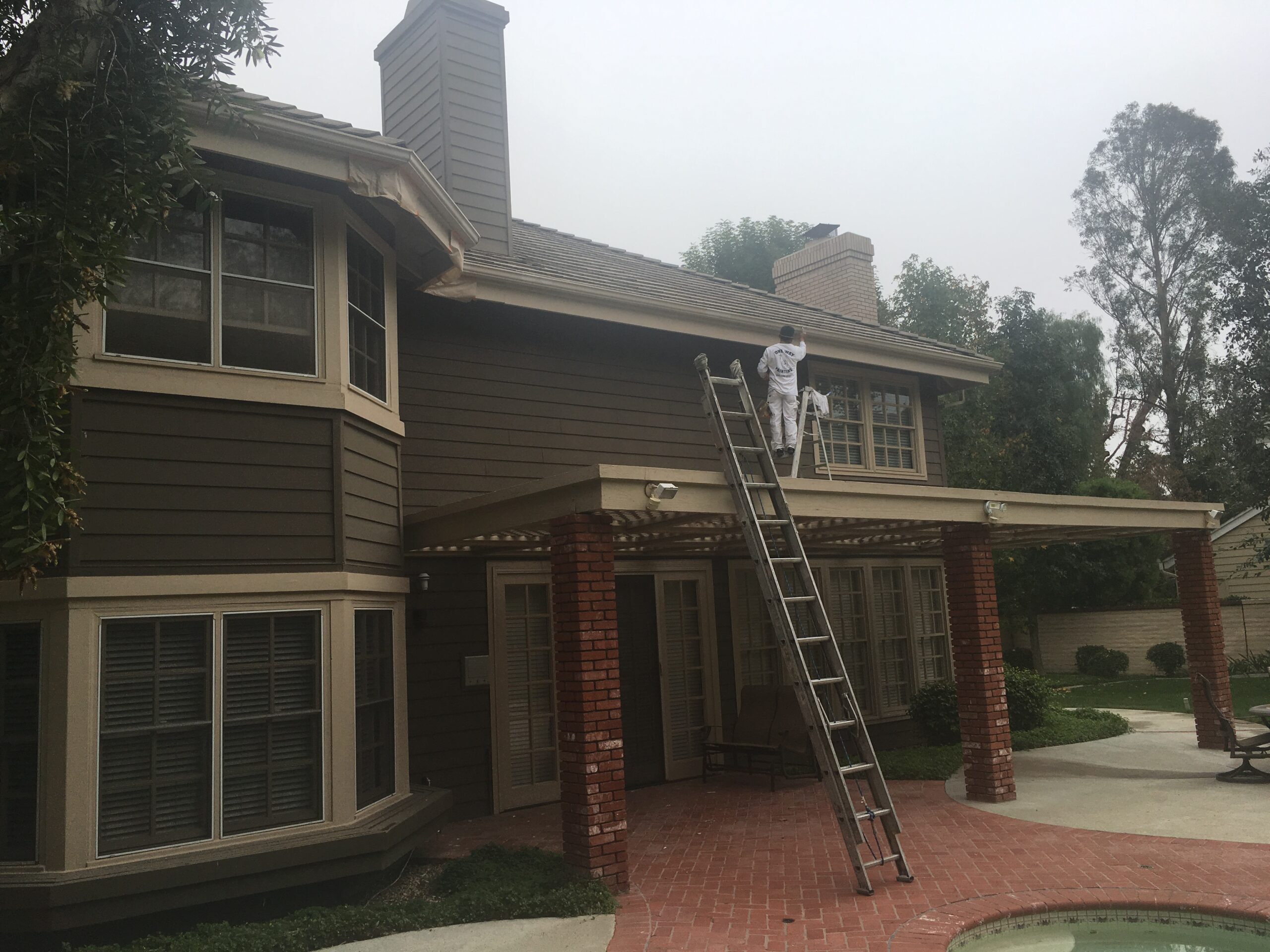 One Way Painting exterior home painter on a ladder while painting a 2-story exterior home in Villa Park, CA.