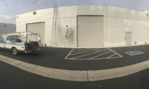 One Way Painting Painters working on the exterior of a commercial building, using ladders and standing next to One Way Painting's company truck.