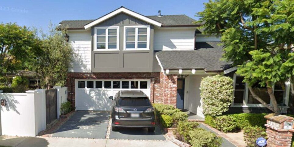 The same two-story home in Costa Mesa CA after our exterior painters completed full painting, with white siding, gray accent color, white window trim, white garage door, white stucco perimeter wall, and deep blue front door.