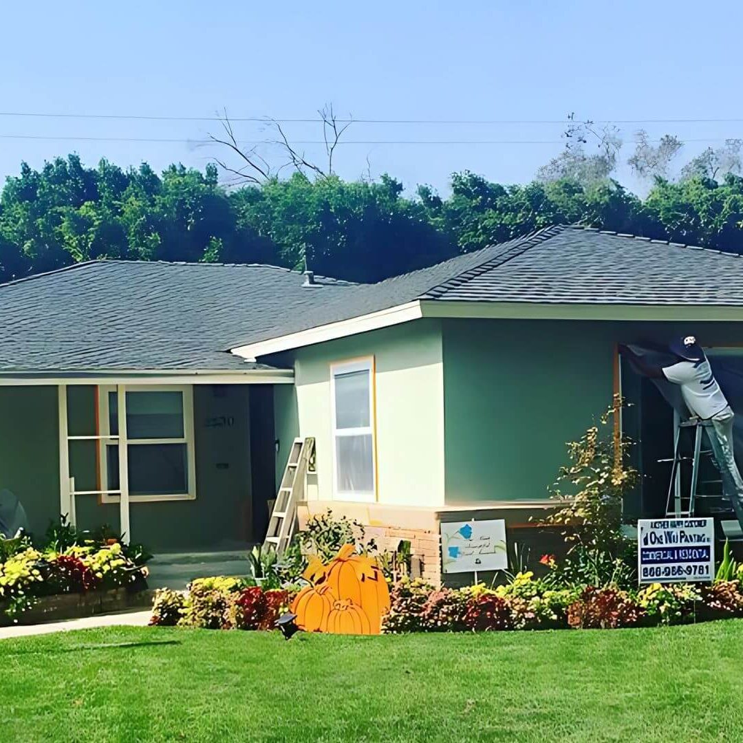 One Way Painting exterior house painter on a ladder masking an exterior window of a house in Santa Ana.