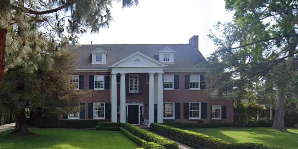 A historic Santa Ana 2-story home with a lush walkway leading up to a beautiful doorway framed by large white column after exterior house painting completed by One Way Painting painters