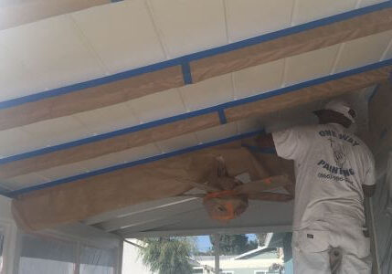 Painter masking the beams under the eaves of a house for painting eaves, using tape and covering nearby areas.