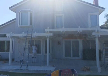 One Way Painting Exterior House Painter working on the exterior of a large two-story house with a patio cover in Laguna Nigel, under bright sunlight.