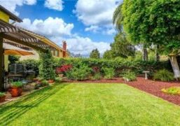 A beautifully maintained backyard featuring a pergola we painted on the patio, surrounded by lush greenery and vibrant flowers, providing a serene outdoor space.